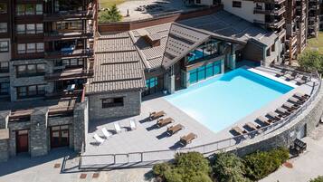 A hotel with a swimming pool, outdoor seating, and a stone facade.