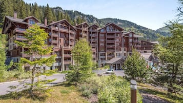 A multi-story hotel with balconies, surrounded by trees and mountains.