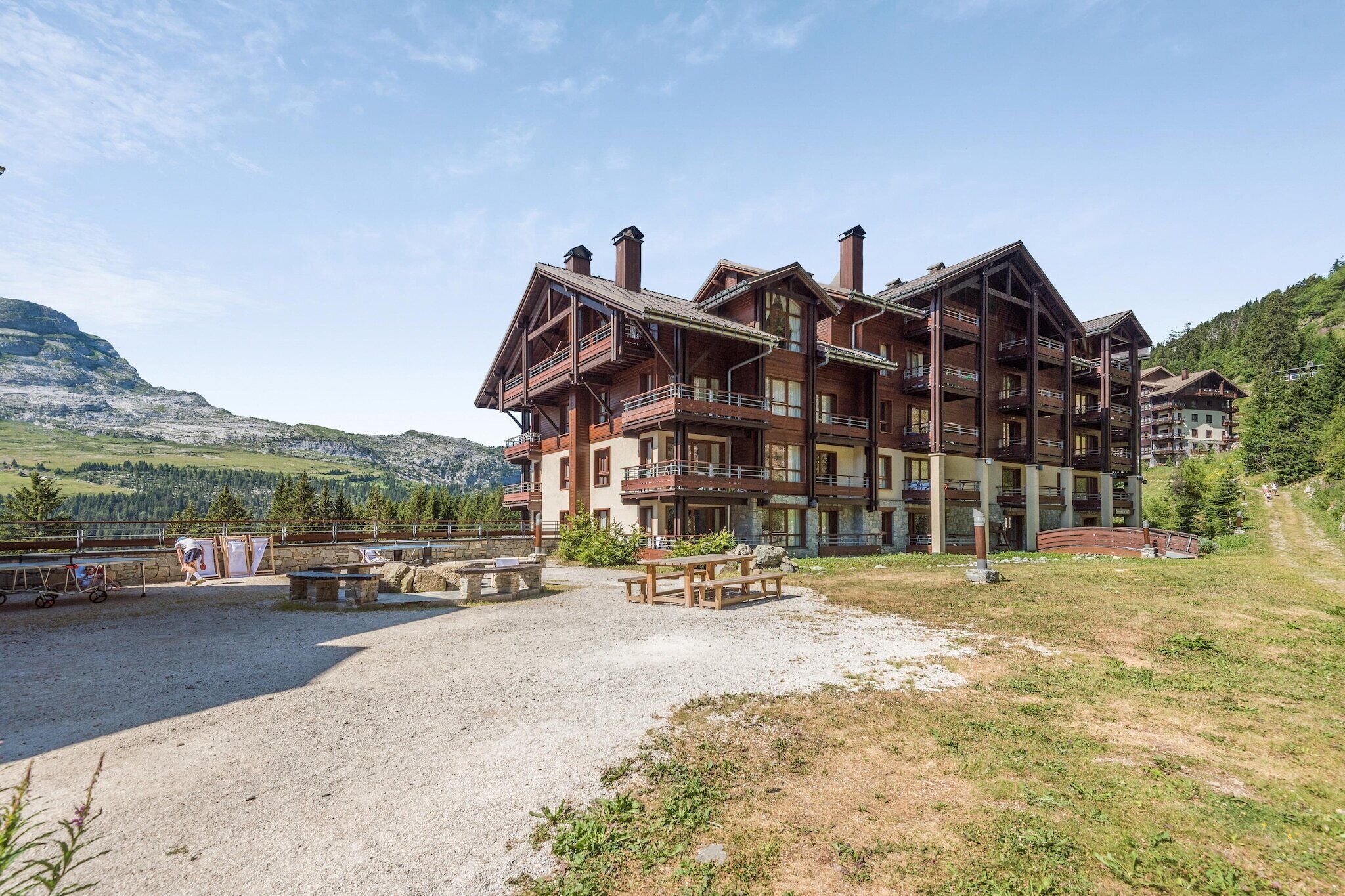 Un hôtel à plusieurs étages doté de balcons, d’une cour en gravier et surplombant un paysage montagneux.