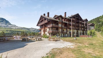 Un hôtel à plusieurs étages doté de balcons, d’une cour en gravier et surplombant un paysage montagneux.
