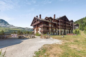 A multi-story hotel with balconies, a gravel courtyard, and a mountainous backdrop.
