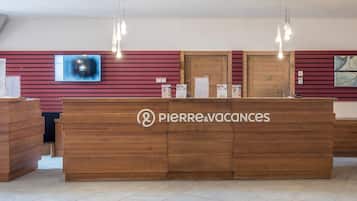 A reception desk with a logo, a mounted TV, and hanging pendant lights.