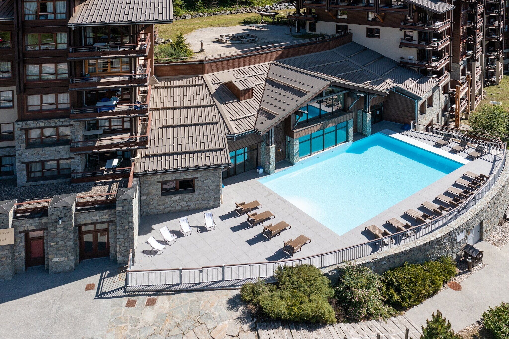 A hotel with a swimming pool, outdoor seating, and a stone facade.