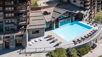 A hotel with a swimming pool, outdoor seating, and a stone facade.