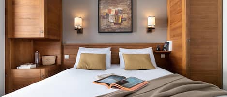 Habitación de hotel con una cama grande, armario de madera, dos lámparas de noche y un cuadro en la pared.