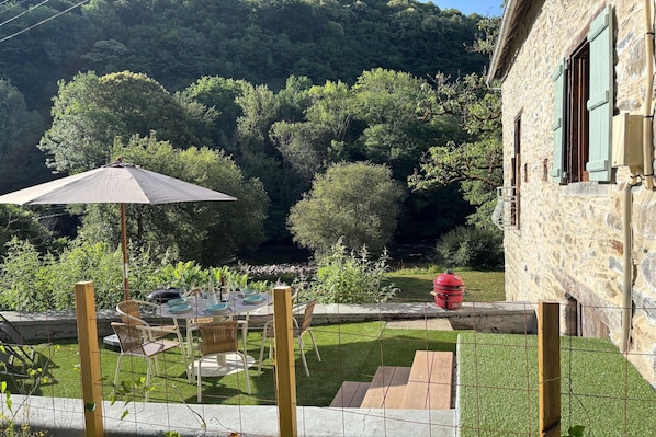 Un patio con una mesa lista para comer, rodeado por un muro de piedra y vistas a una ladera boscosa.