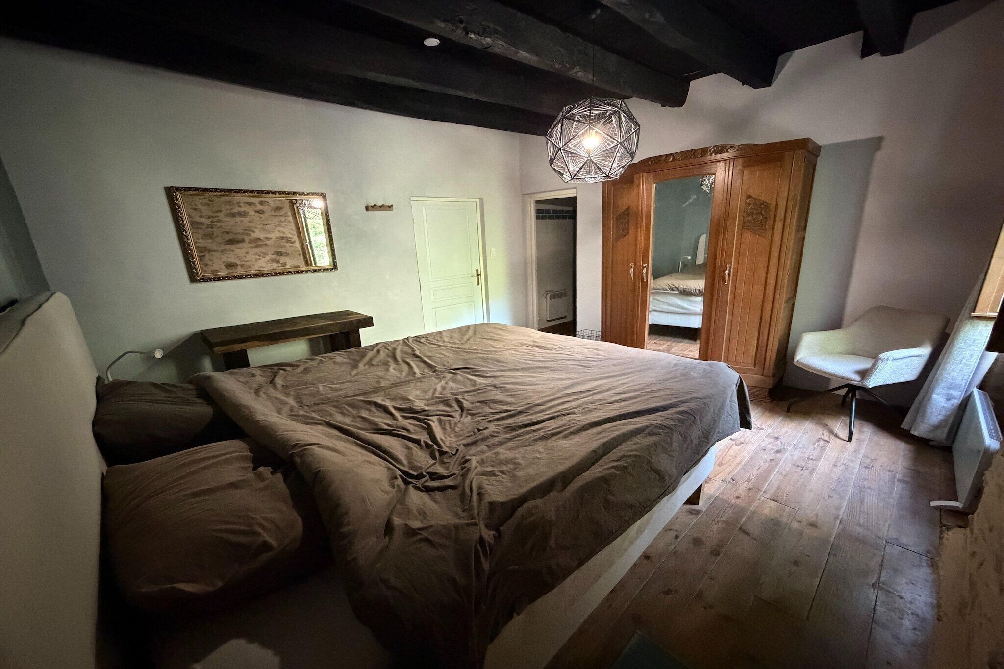 Une chambre à coucher comprenant un lit, un banc en bois, un luminaire suspendu et une armoire.