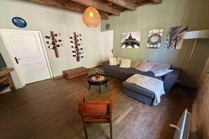 Una sala de estar con sofá, una mesa de centro, una silla de madera, una lámpara colgante y estanterías para vino en la pared.
