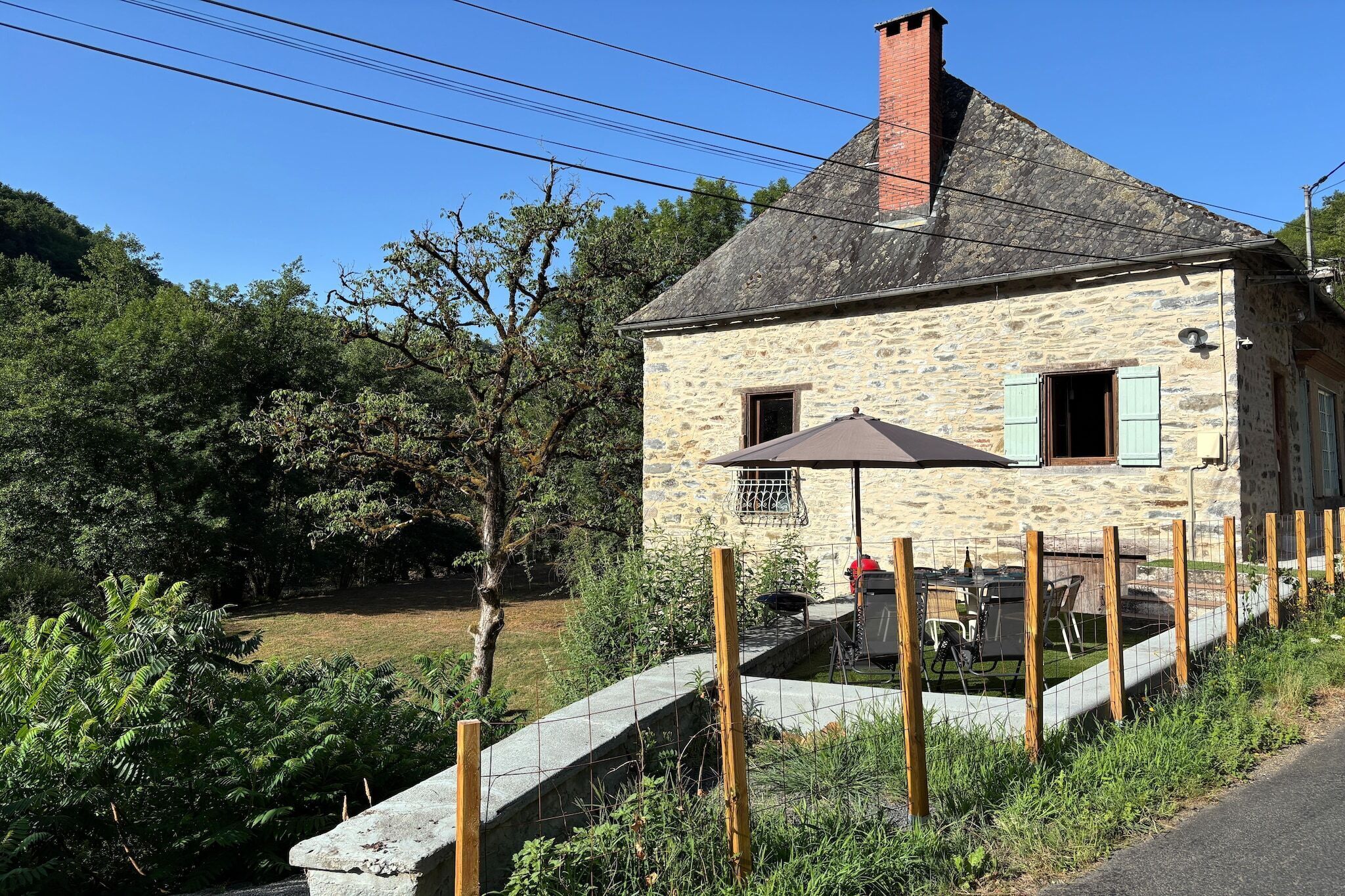 Een stenen huis met schoorsteen, een balkon met metalen hekwerk, en een tafel met stoelen buiten.
