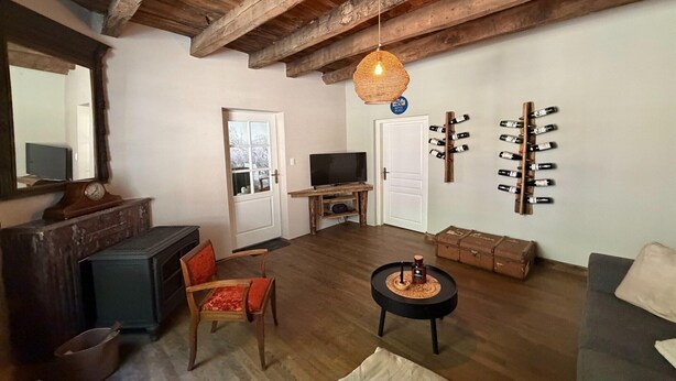 Ein rustikaler Raum mit Holzbalkendecke, einem Fernseher auf einem Holzständer, einem Weinregal und einem alten Koffer.