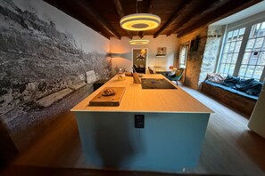 A modern kitchen with a central island, a stone wall mural, and a seating area with a view. - Comfortable and authentic holiday home in Orgnac-sur-Vézère on the Vézère (Orgnac-sur-Vézère)