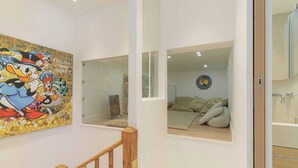 A room with a wooden staircase, a bed with pillows, a wall with a cartoon character mural, and a window with a view of another room. - 1BDR/3P flat - balcony - in the heart of Deauville (Deauville)