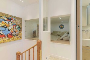A room with a wooden staircase, a bed with pillows, a wall with a cartoon character mural, and a window with a view of another room. - 1BDR/3P flat - balcony - in the heart of Deauville (Deauville)