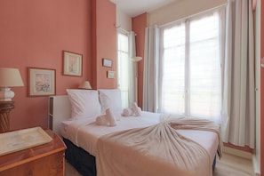 A hotel room with a bed, a bedside table, a lamp, and a window with curtains. - Flat in a traditional Norman townhouse – Garden (Deauville)