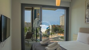 A hotel room with a bed, a TV, a chair, and a view of the city through a glass door. - CostaBlancaDreams - Arenal Beach 10 in Calpe (Calpe / Calp)
