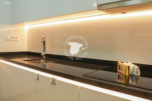 Uma cozinha moderna com bancada preta, pia de aço inoxidável e um logotipo no painel da parede.