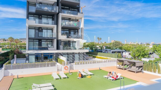 A modern multi-story building with balconies, a rooftop pool area with sun loungers, and a view of the cityscape. - CostaBlancaDreams - Arenal Beach 10 in Calpe (Calpe / Calp)