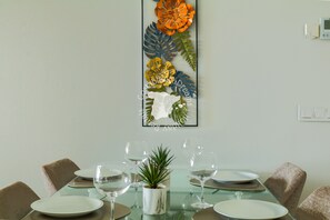 Uma área de jantar com mesa de vidro posta para quatro pessoas, rodeada por cadeiras.