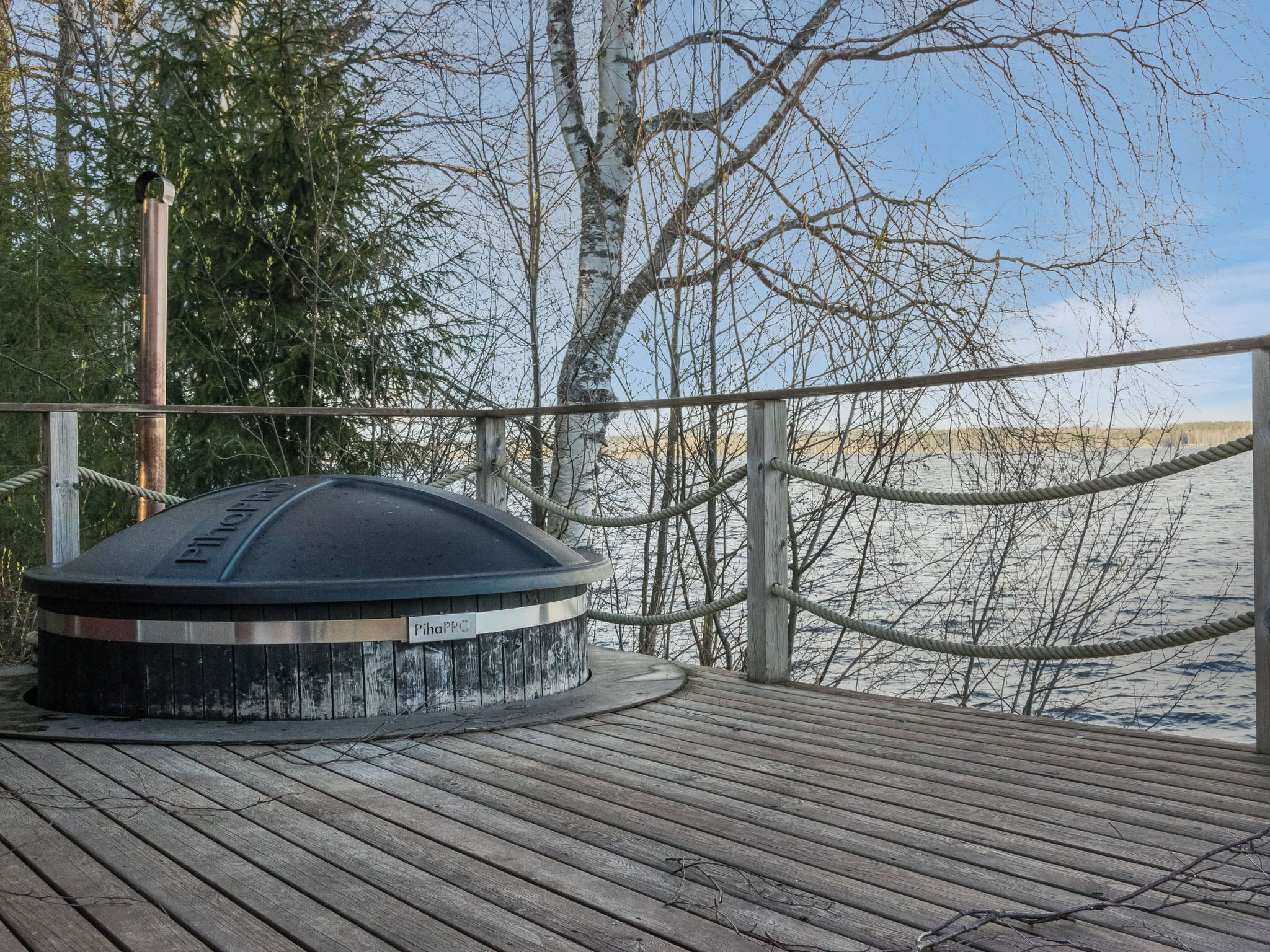 A wooden deck with a sauna, surrounded by trees and a view of a body of water.