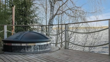 A wooden deck with a sauna, surrounded by trees and a view of a body of water.
