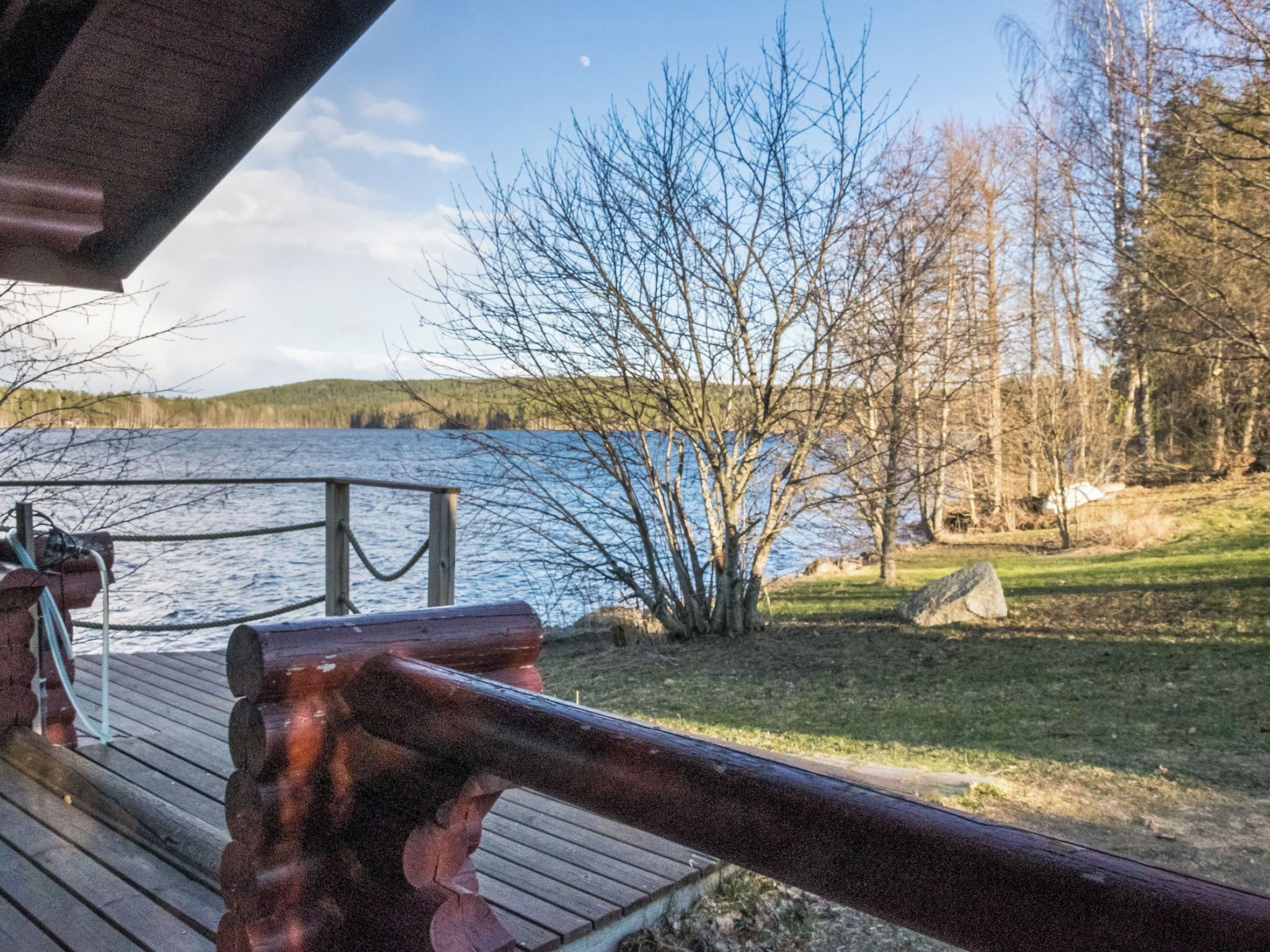 A wooden deck with a metal railing overlooking a lake, surrounded by trees and a grassy area.