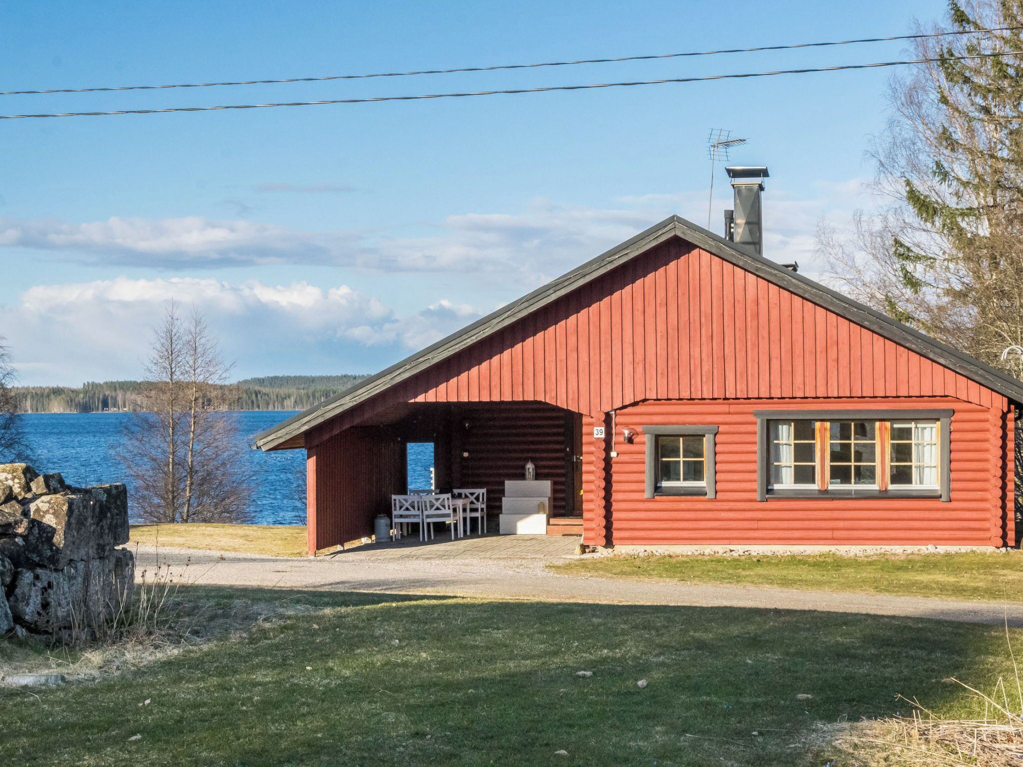 Una cabaña de madera roja con un porche pequeño, una chimenea y vistas a un lago.