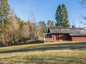 Una cabana vermella de fusta amb un teulat inclinat, envoltada per un camp verd i arbres alts.