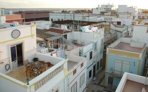 Un edificio residencial de varios pisos con balcones, un comedor con mobiliario exterior y vista al mar.
