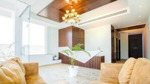 Un interior moderno con techo de madera, una lámpara de araña, un mostrador de recepción y una zona de estar con una planta en maceta.