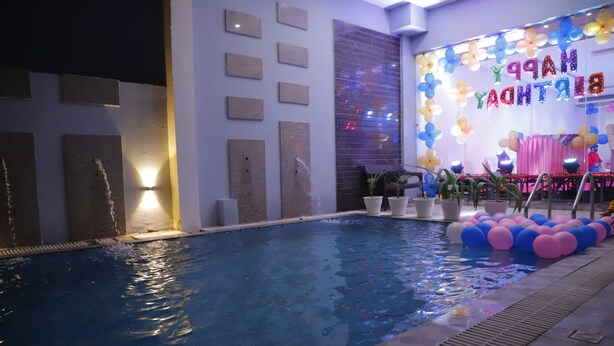 Una piscina interior con un cartel que dice 'Feliz Cumpleaños', plantas en macetas y un escenario con un fondo rosa.
