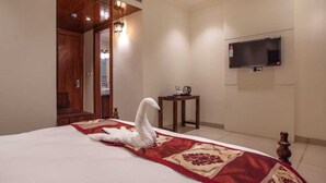 Habitación de hotel con cama, televisor montado en la pared, una mesita con hervidor y una puerta de madera.