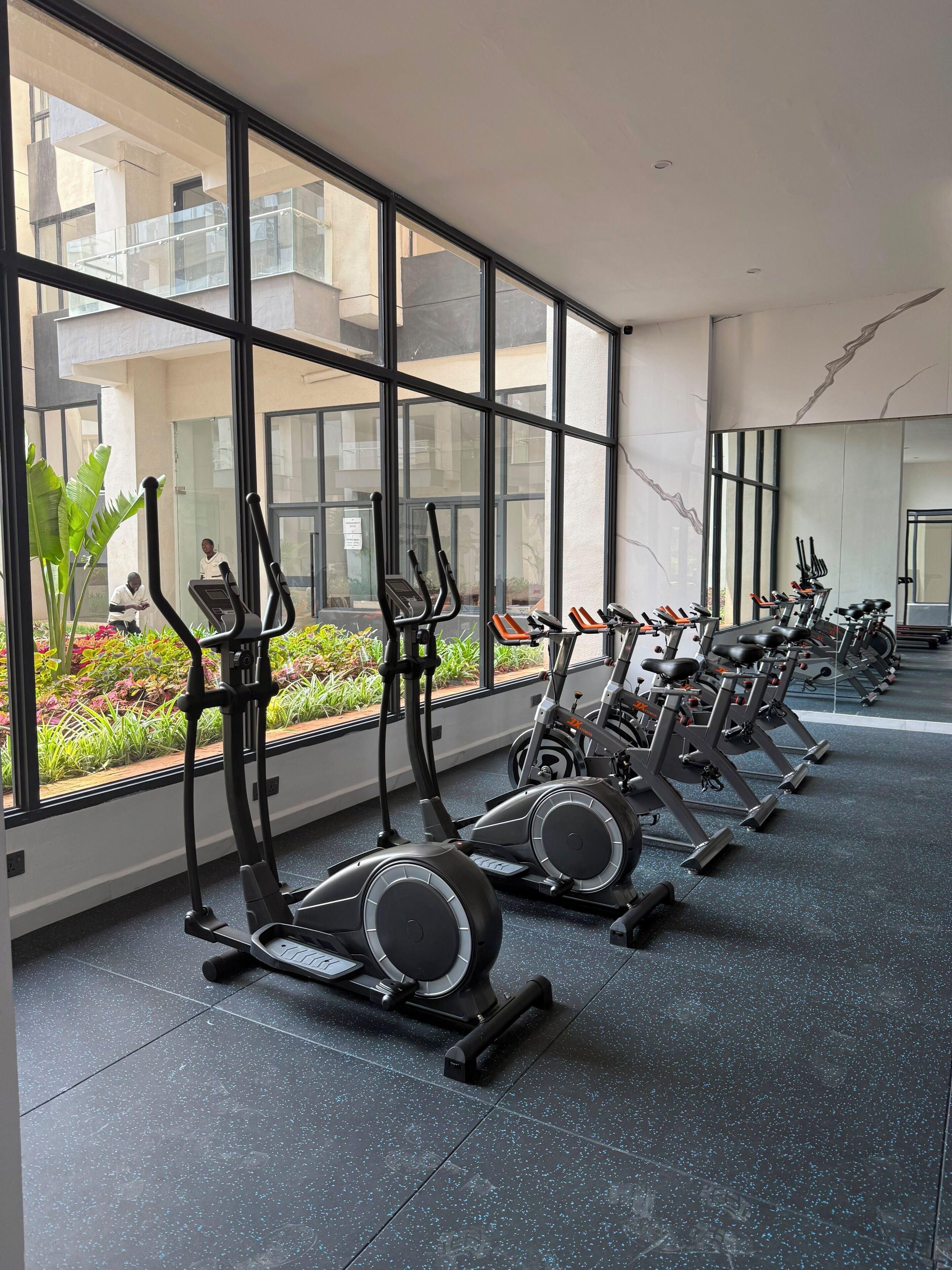 Ein Fitnessraum mit Ergometer und Laufbändern, großen Fenstern und Blick auf ein Gebäude.