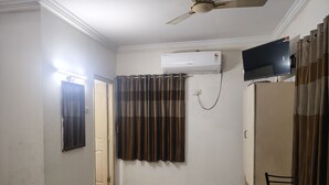 A room with a ceiling fan, an air conditioning unit, a television, and a chair. - VIP Residency (Tirupati)