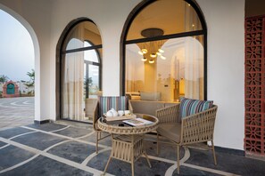 A seating area with wicker chairs and a table, a large window with curtains, and a view of the outside. - ELIVAAS Prive Heaven 6BHK Villa wth Pool (Sohna)
