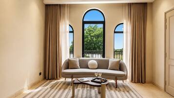 A room with a sofa, a coffee table, and a view through large windows.