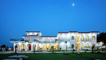 A large, multi-story building with a symmetrical facade, multiple balconies, and a well-maintained lawn.