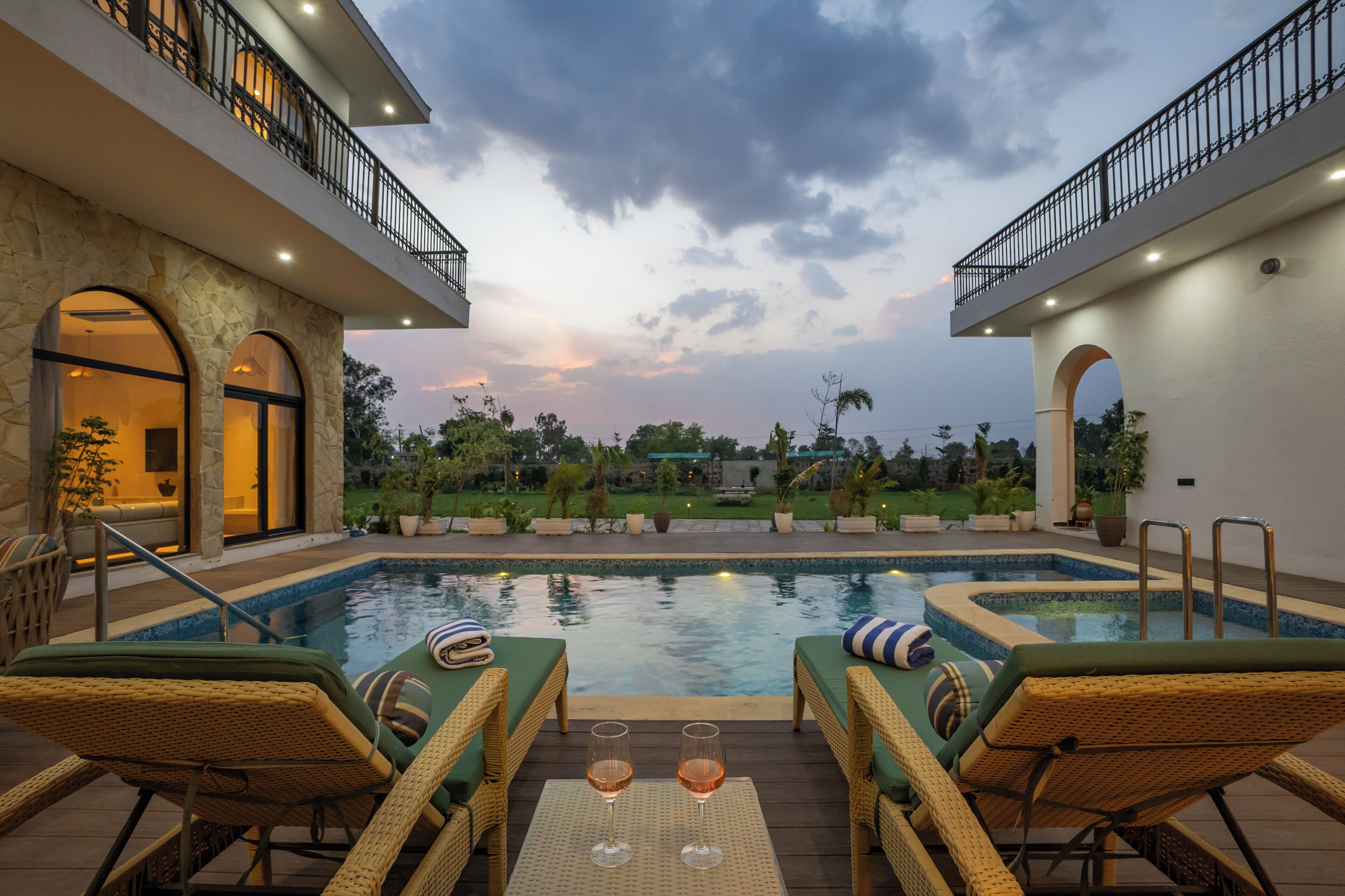 Un espace piscine avec des chaises longues et une coupe de vin, entouré d’un jardin aménagé et d’un bâtiment doté de balcons.