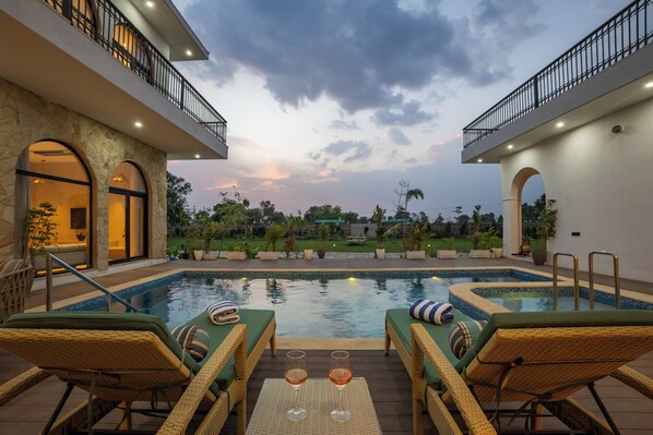 A pool area with lounge chairs and a glass of wine, surrounded by a landscaped garden and a building with balconies.