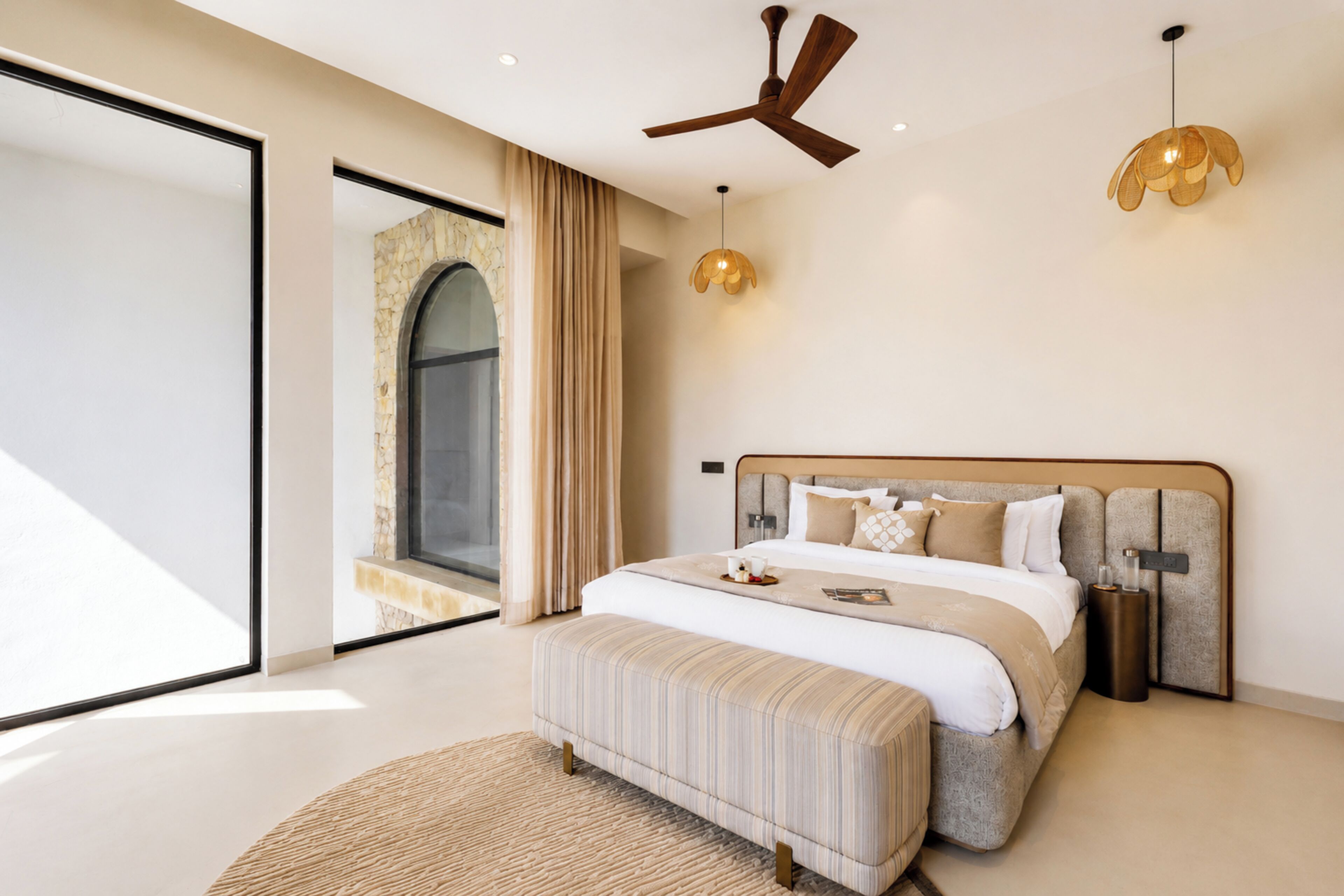 Un dormitorio moderno con una cama grande, un ventilador de techo y vistas a un arco de piedra.