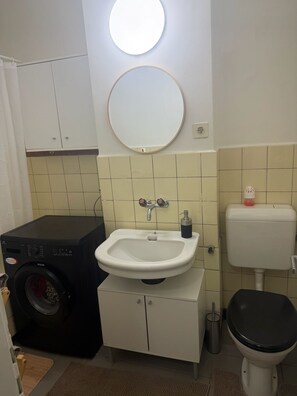 Une petite salle de bain comprenant un lavabo, des toilettes et un lave-linge.
