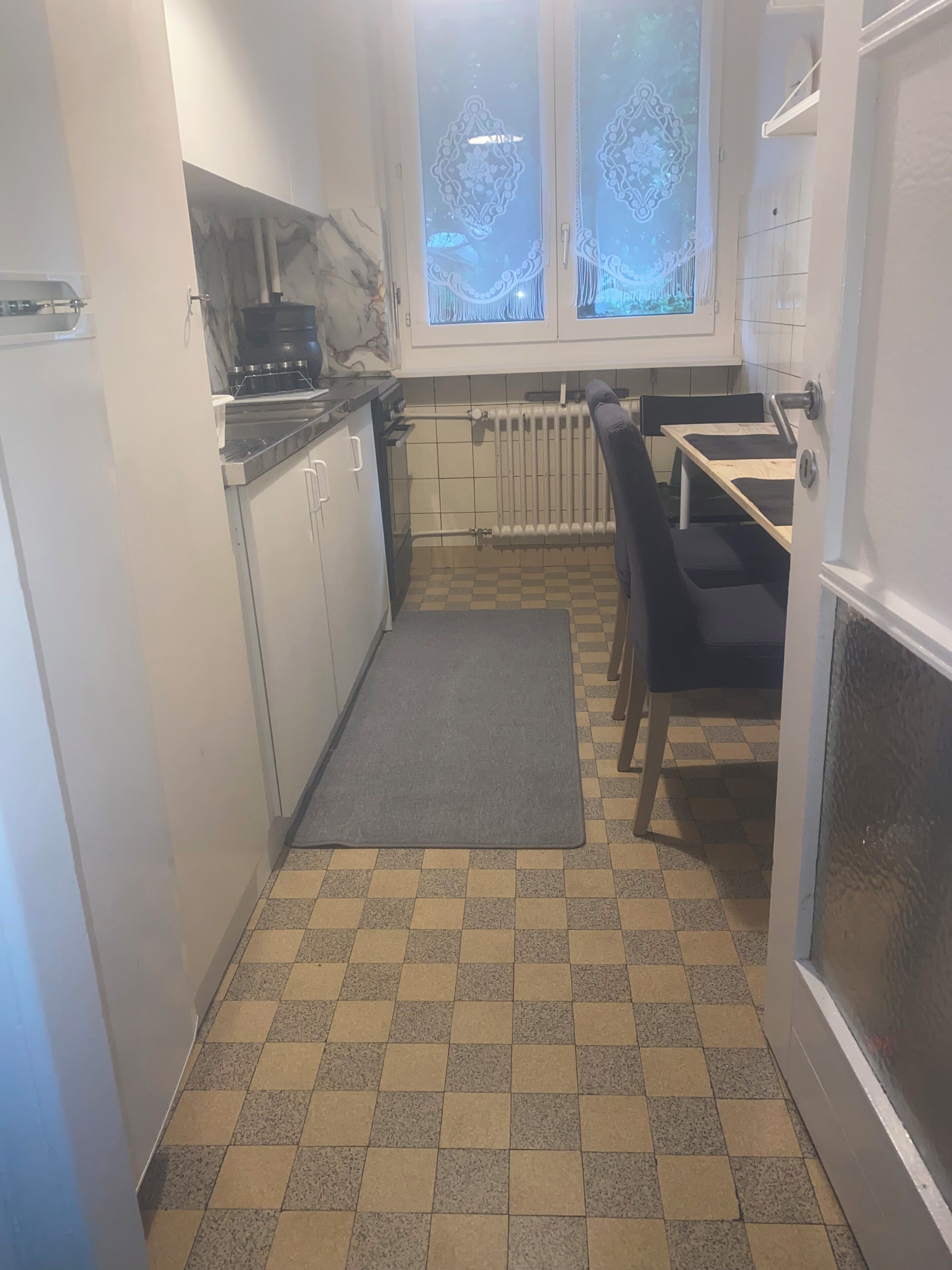 A compact kitchen with a checkered floor, a radiator, and a window with frosted glass.