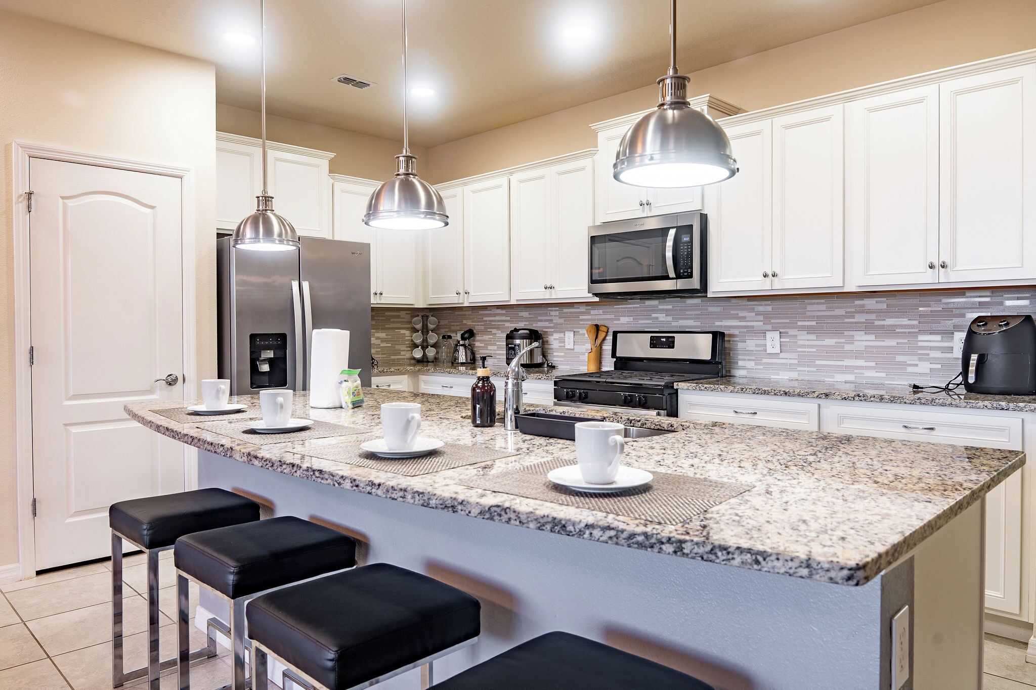Una cocina moderna con una isla central, taburetes de bar, electrodomésticos de acero inoxidable e iluminación colgante.