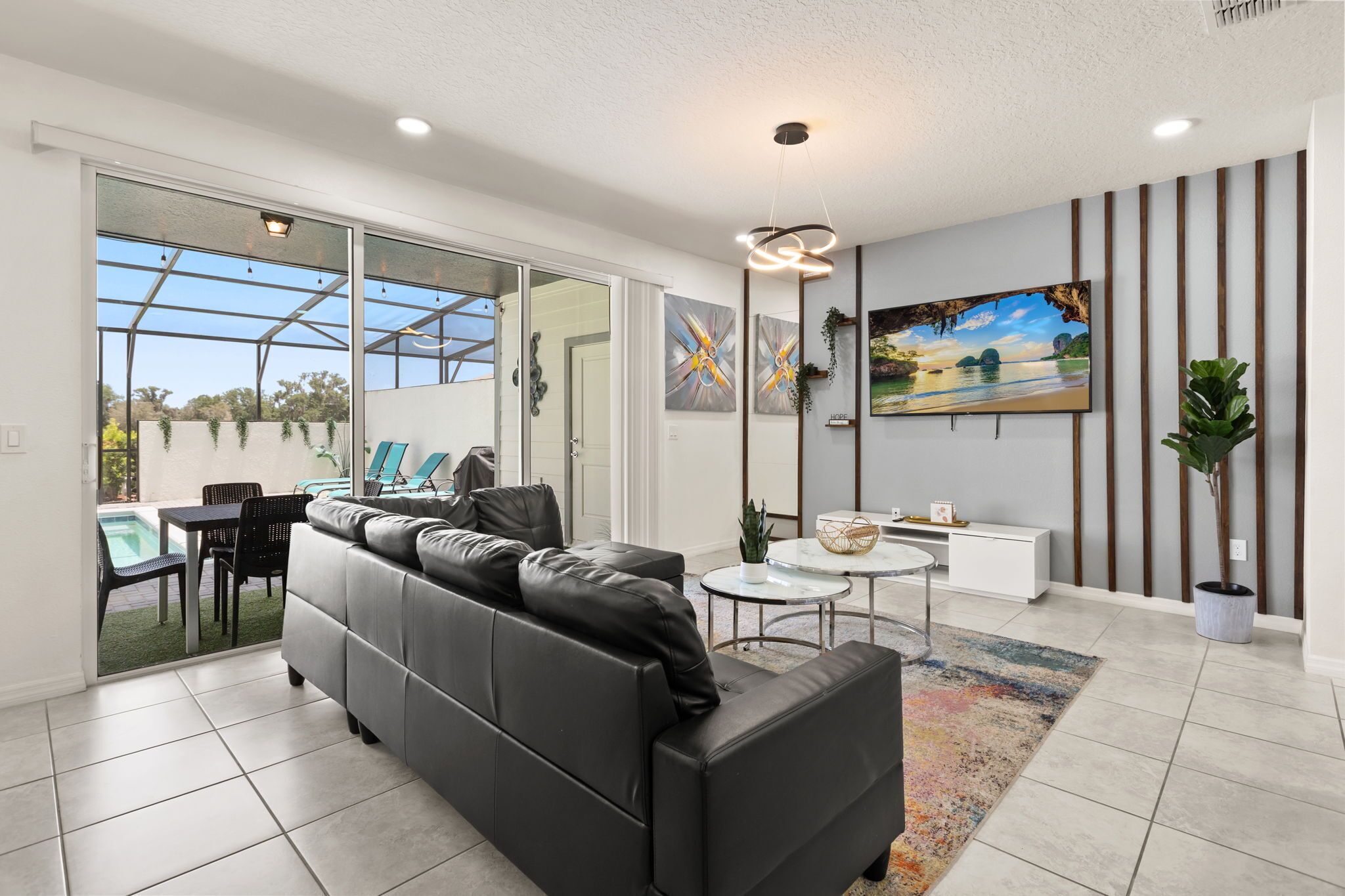 A modern living room with a black leather sofa, a TV, and a glass door leading to a patio with outdoor furniture.