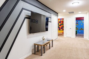 A hallway with a flat-screen TV mounted on the wall, a small table with a globe and pen, and a colorful play area with a Mario-themed wall. - Book Your Christmas Stay/Your Holiday Gift Awaits! (Davenport)