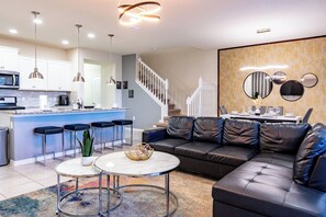 A modern living room with a black leather sofa, a dining table set for four, and a kitchen area with a bar. - Book Your Christmas Stay/Your Holiday Gift Awaits! (Davenport)