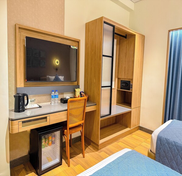 A hotel room with a desk, a chair, a mini-fridge, a bed, a wardrobe, and a mirror.