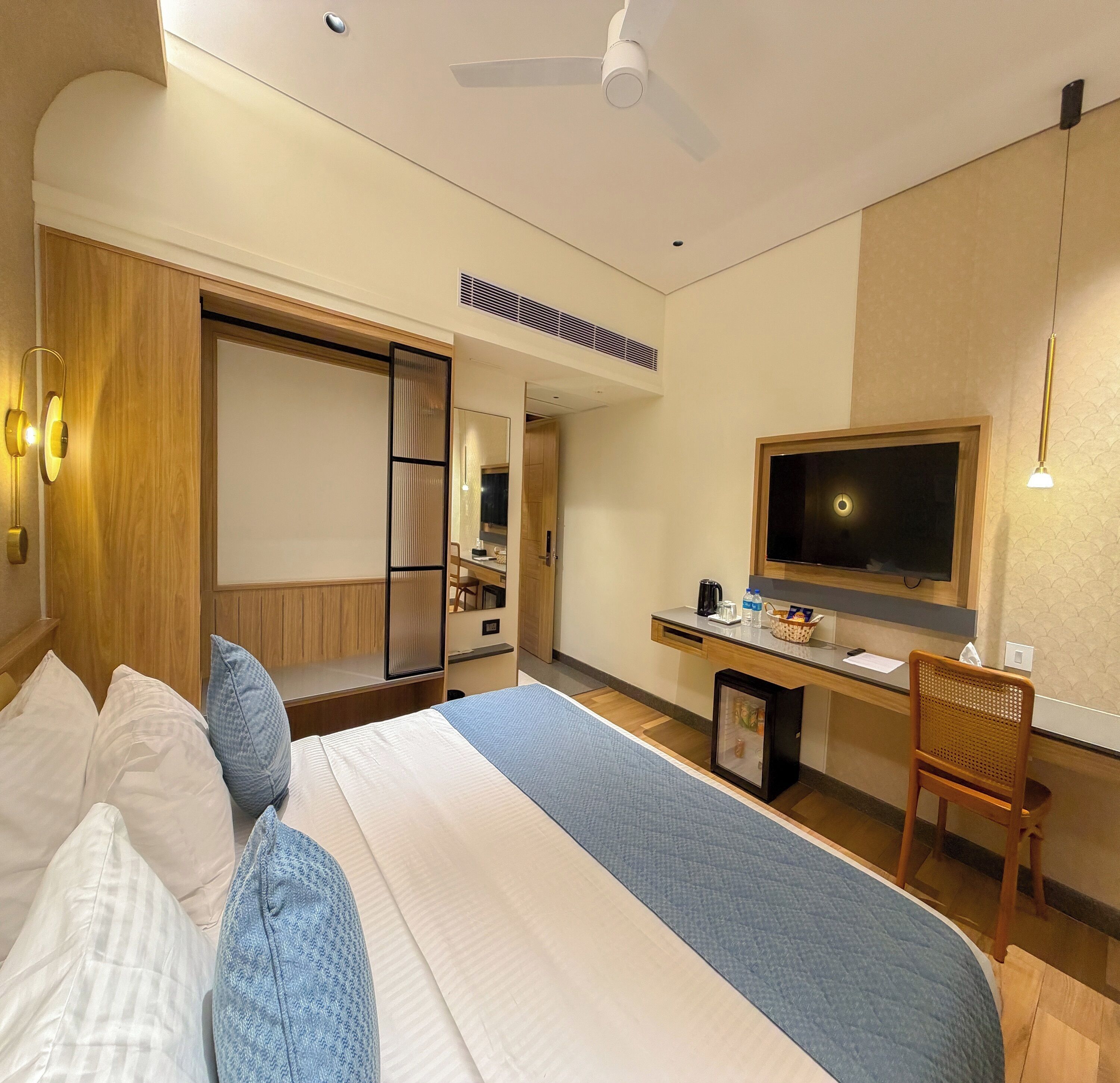A hotel room with a bed, a desk, a chair, a television, and a ceiling fan.