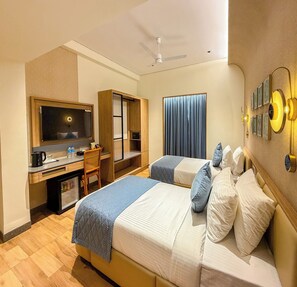 Habitación de hotel con cama, escritorio, silla, televisor y ventilador de techo.