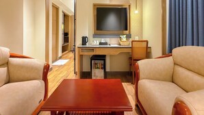 Habitación de hotel con un escritorio de madera, televisor, cafetera y dos sillones.