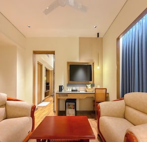 A hotel room with a wooden desk, a television, a coffee maker, and two armchairs. - A1 Diya Palace (Sankarankovil)